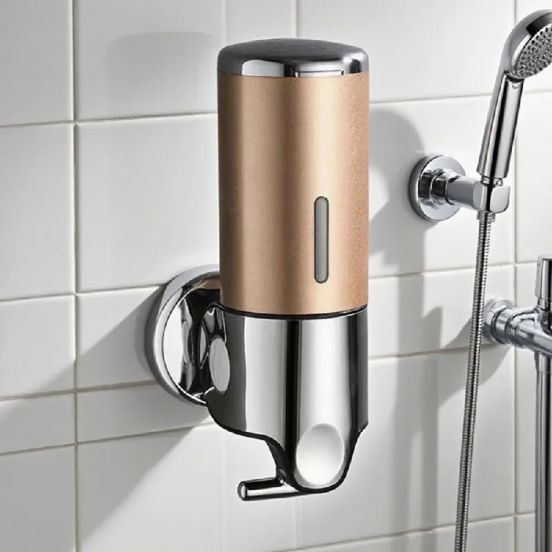 Wall-mounted soap dispenser with gold and silver design on a tiled bathroom wall.